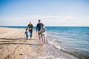 Young family with two small children running barefoot outdoors on beach.