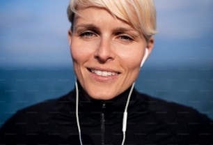 Front view portrait of young sportswoman with earphones standing outdoors on beach.