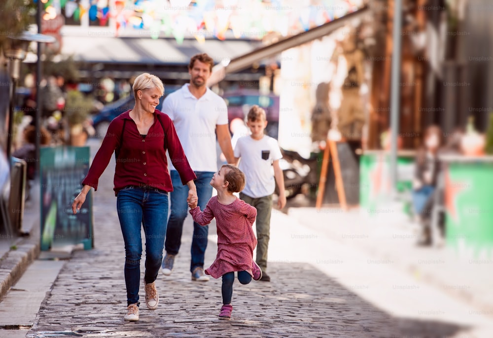 Happy young family with two small children walking outdoors in town on holiday, talking.