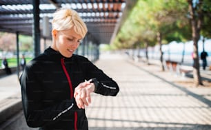 A portrait of young sportswoman with smartwatch resting after doing exercise outdoors. Copy space.