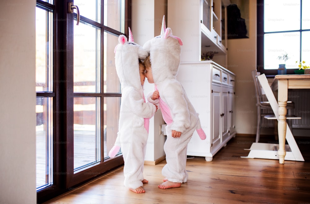 Two toddler children with white unicorn masks playing indoors at home.