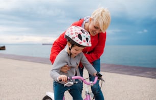 Young mother helping small daughter to ride bicycle outdoors on beach.