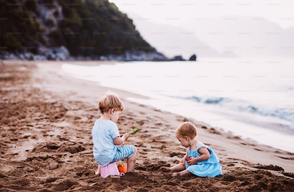 Two toddler children playing on sand beach on summer family holiday.