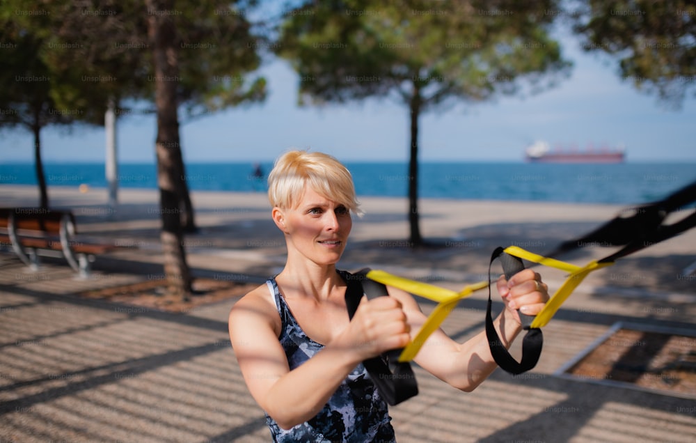 Una atractiva joven deportista haciendo ejercicio con correas de fitness al aire libre.
