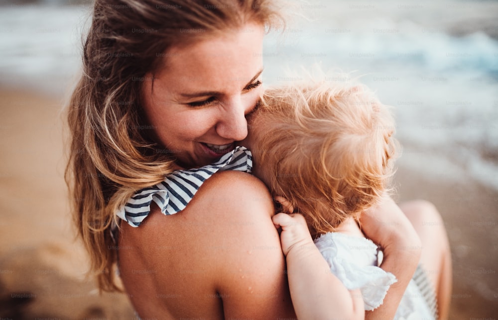 A close-up of young mother with a toddler girl on beach on summer holiday.