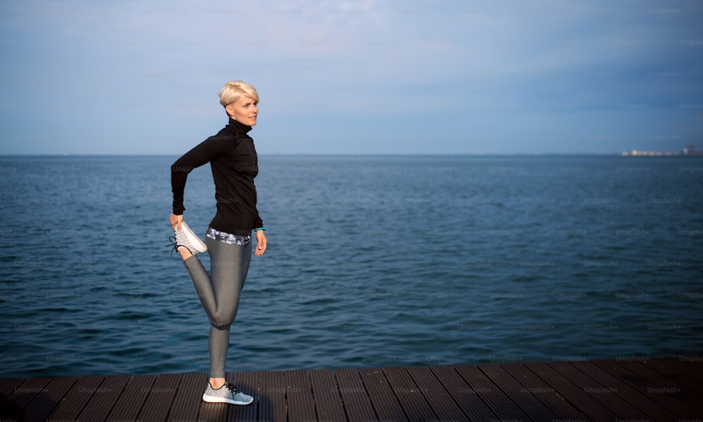 Retrato de vista lateral de una joven deportista de pie al aire libre en la playa, estirándose. Espacio de copia.