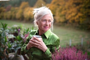 A senior woman with coffee standing outdoors on terrace, resting.