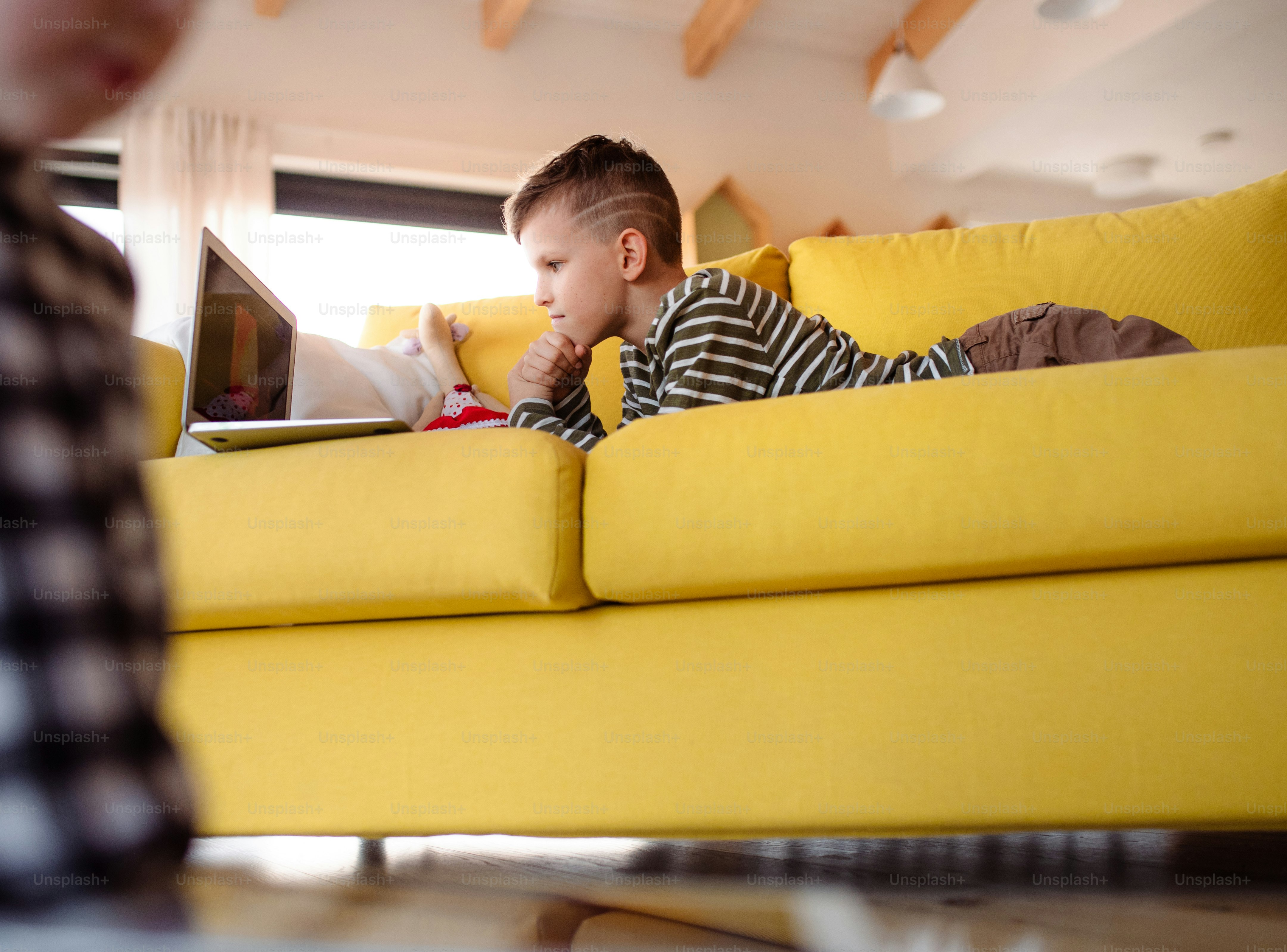 A small boy lying indoors on a sofa at home, using laptop computer.