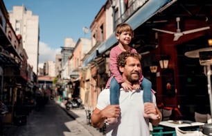 Father with small daughter standing outdoors on street in mediterranean town, giving a piggyback ride.