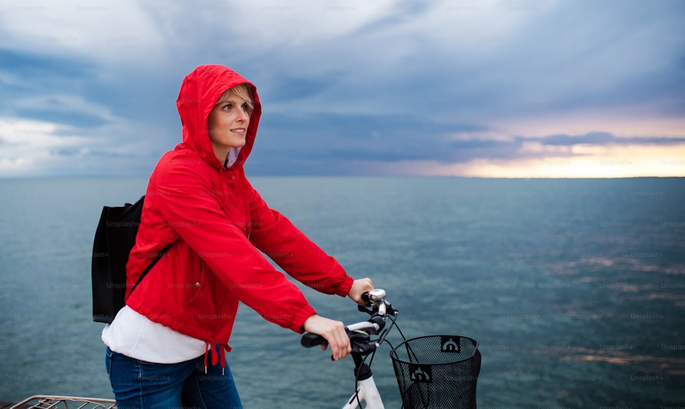 Side view of woman with bicycle standing outdoors on beach, resting. Copy space.