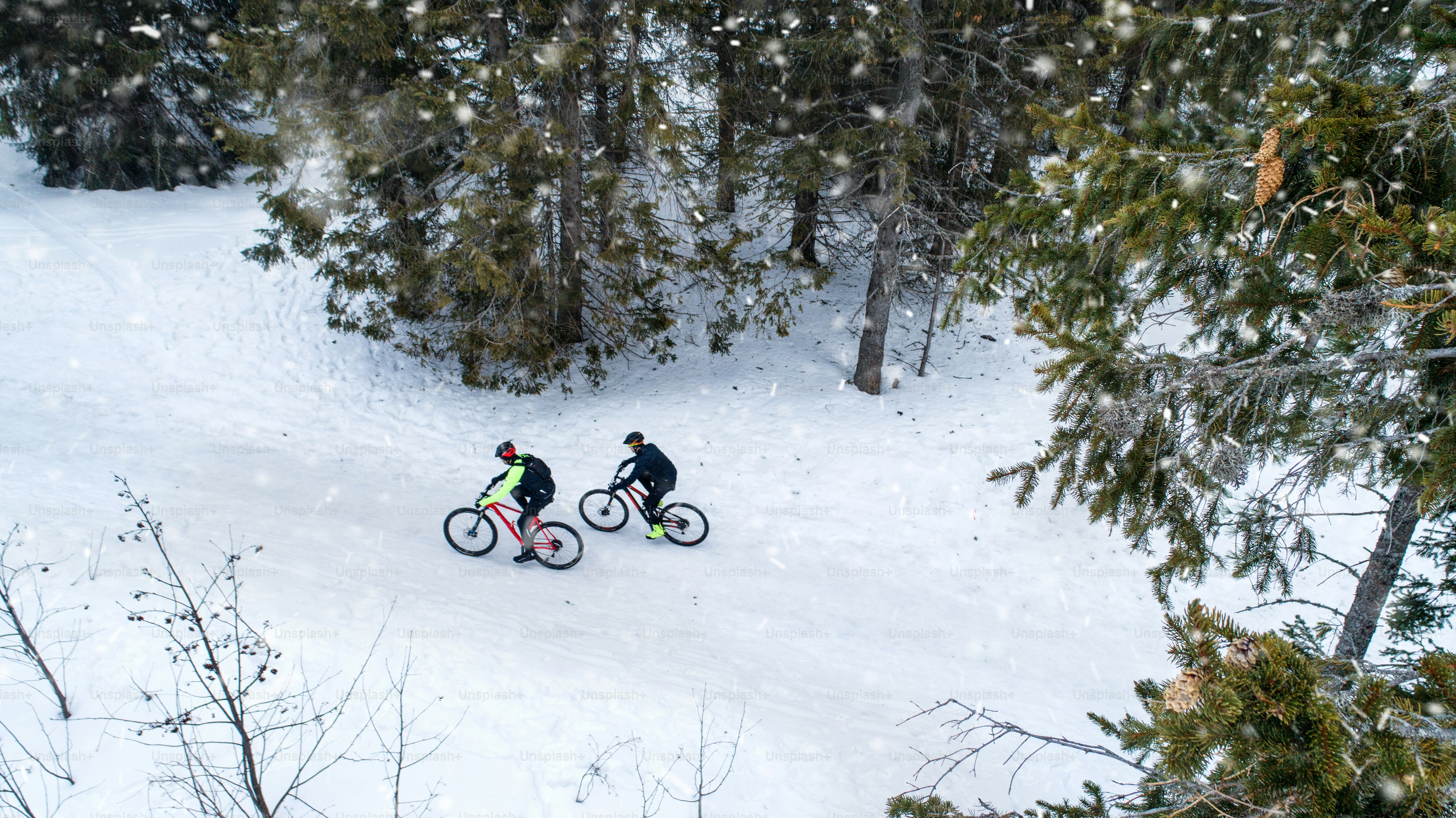 Aerial view of two mountain bikers riding on road covered by snow in forest outdoors in winter.