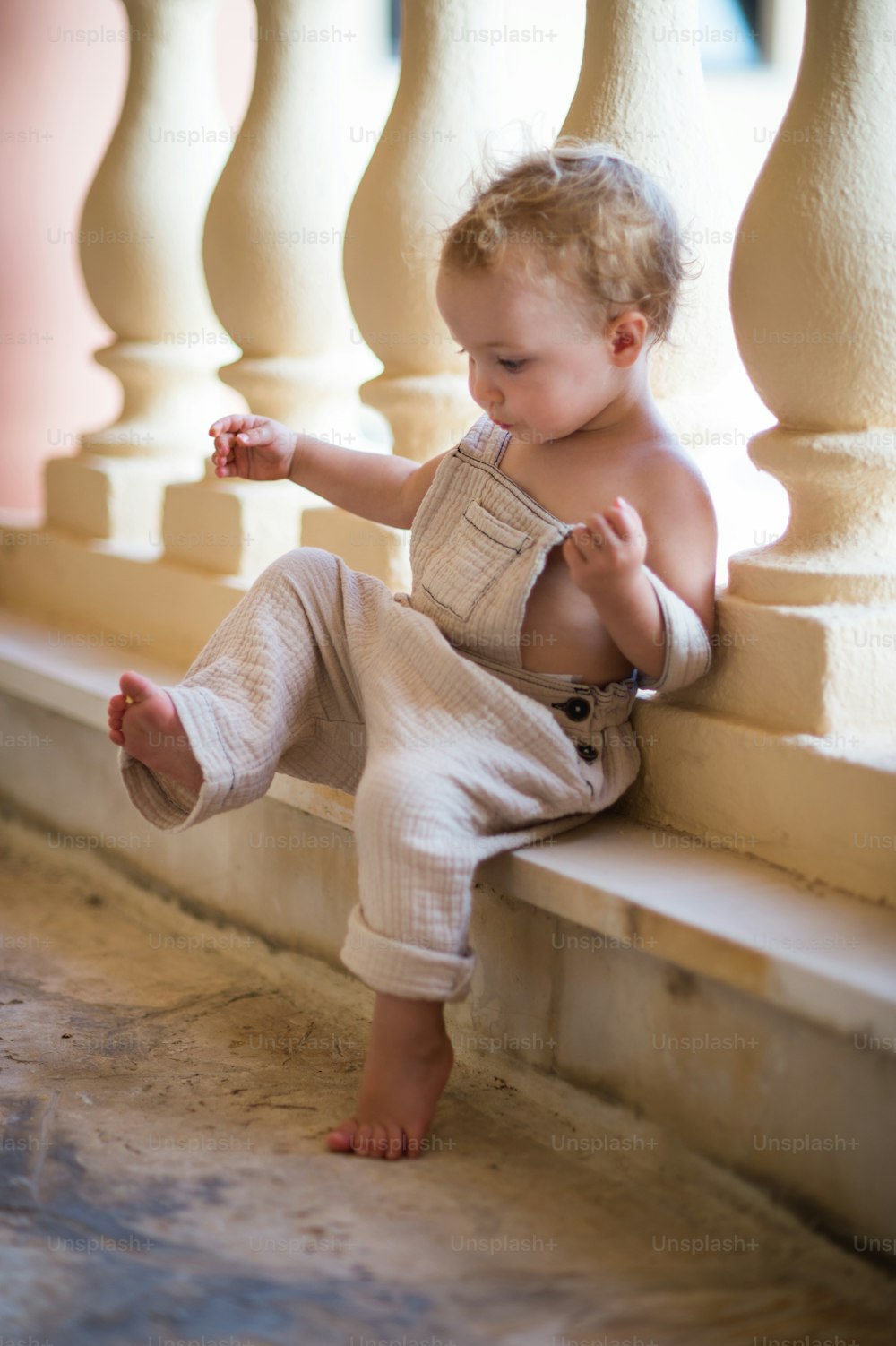 Um retrato de uma menina pequena sentada na frente de grades de concreto ou balaustrada nas férias de verão.