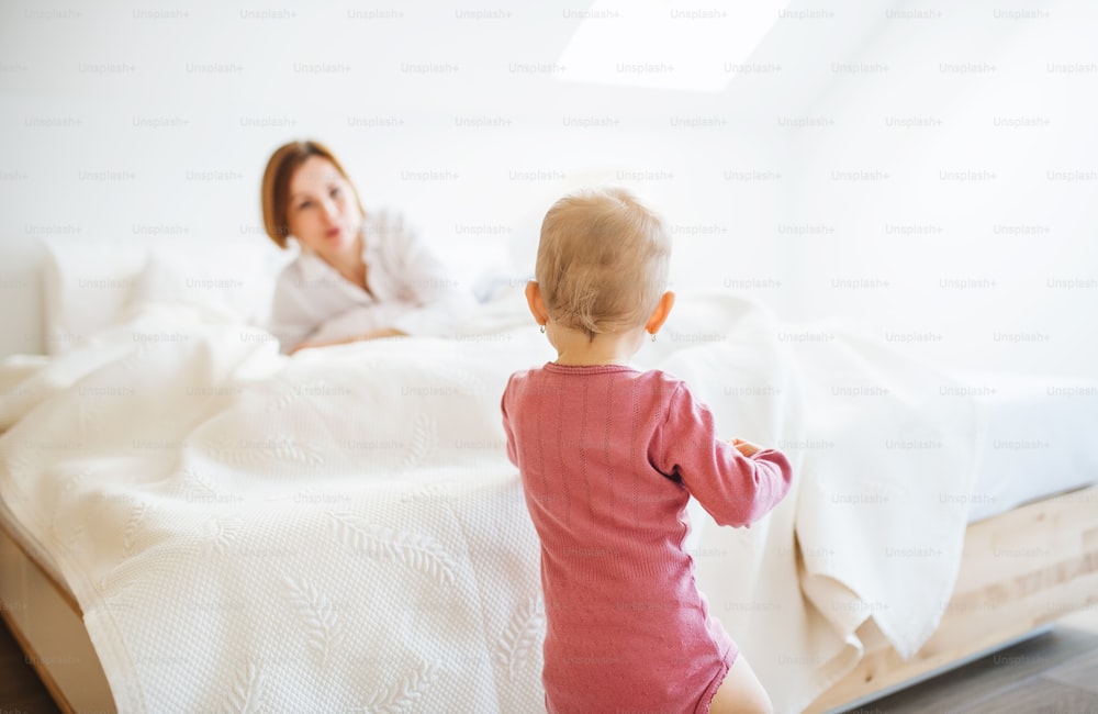 Une jeune mère heureuse avec sa petite fille à l’intérieur sur son lit le matin, en train de jouer.