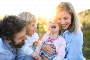 Front view of family with two small children laughing outdoors in spring nature at sunset.
