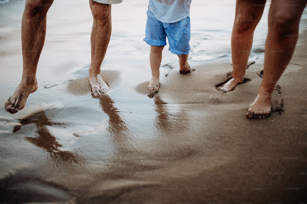 Uma seção intermediária de pais com filha pequena em pé na praia nas férias de verão.