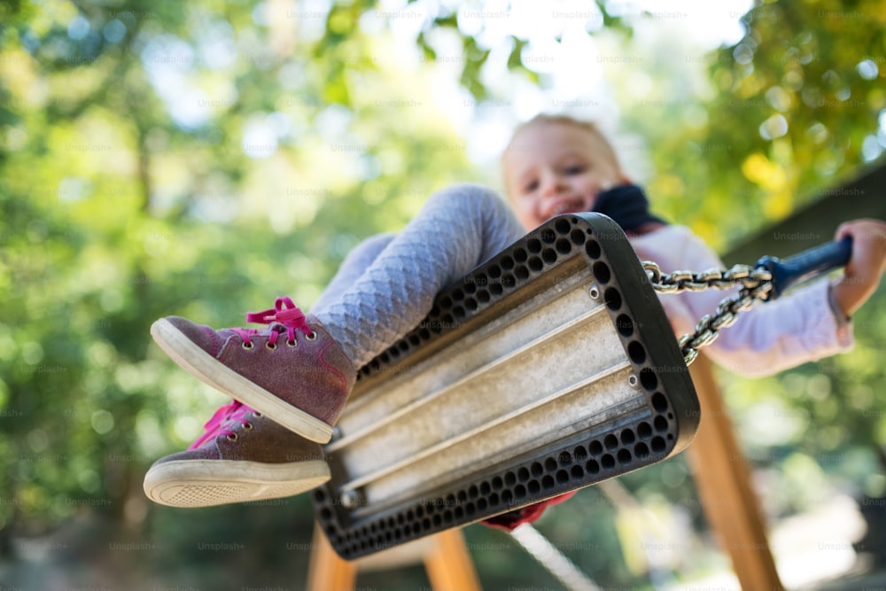 A low angle view of a small toddler girl on a swing on a playground.