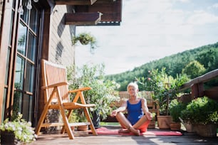 Una donna anziana seduta all'aperto su una terrazza in estate, facendo esercizio di yoga. Copia spazio.