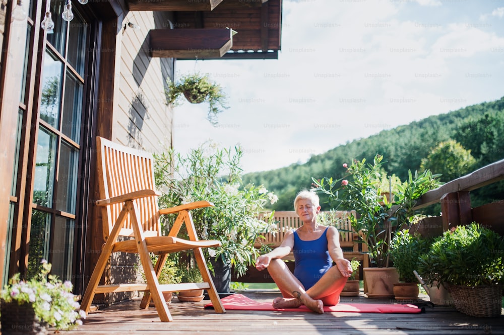 A senior woman sitting outdoors on a terrace in summer, doing yoga exercise. Copy space.