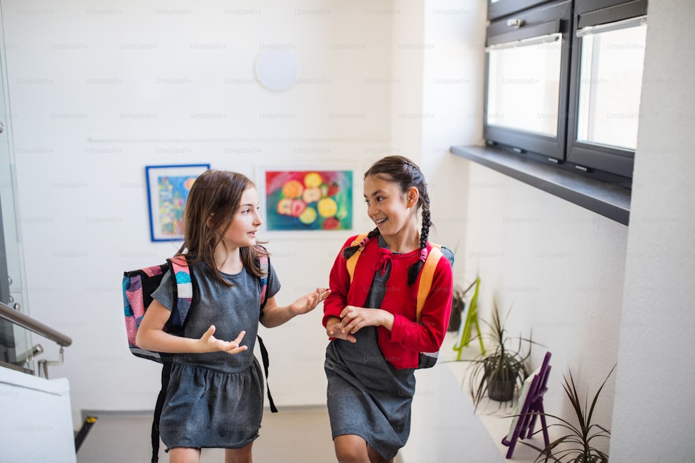 Deux joyeuses petites amies écolières avec des sacs qui montent les escaliers et parlent. Concept de rentrée scolaire.