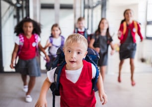 A down-syndrome school boy with bag and group of children in corridor, running.