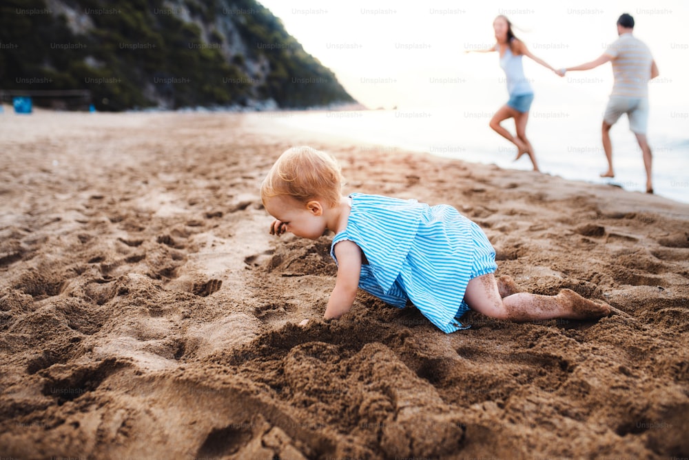 A small toddler girl playing in sand on beach on summer holiday. Copy space.
