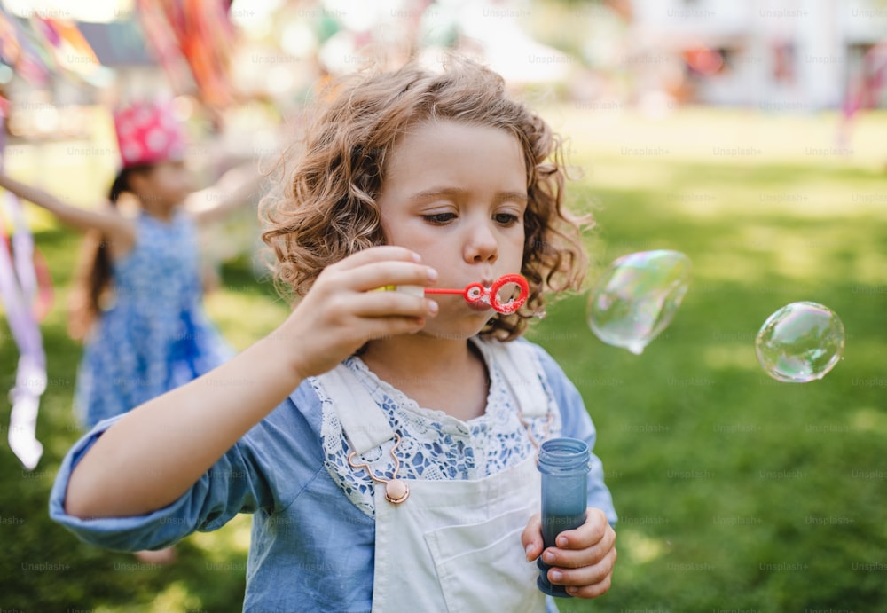 Small girl blowing bubbles outdoors in garden in summer, birthday celebration concept.