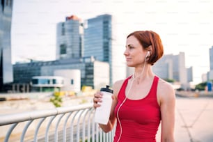 Young woman runner with water bottle in city, resting on the bridge. Copy space.