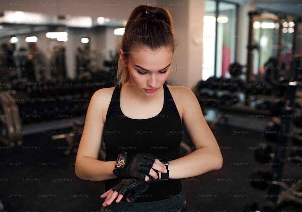 Young girl or woman putting on fingerless gloves in gym.