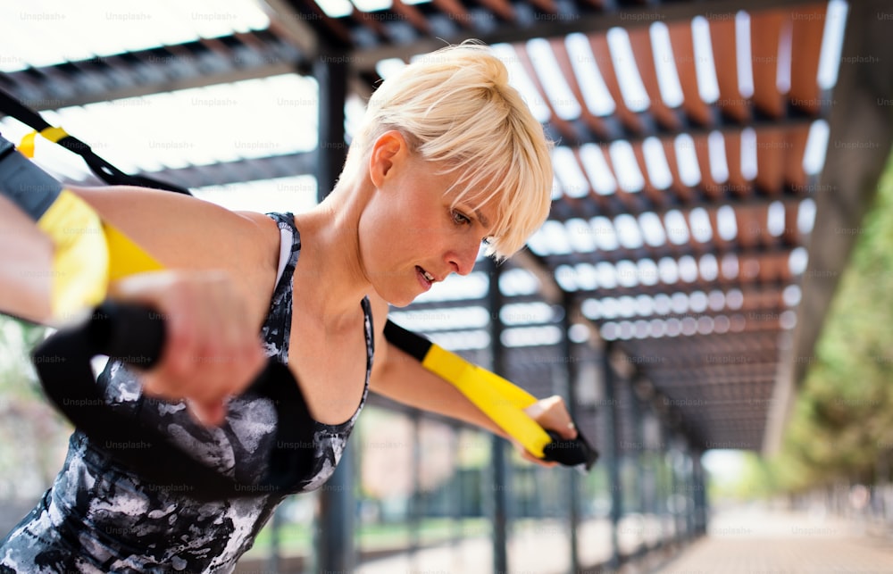 Una atractiva joven deportista haciendo ejercicio con correas de fitness TRX al aire libre.