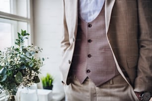 Ein Mittelteil eines Mannes mit formellem Anzug, der auf einer Indoor-Party steht, die Hände in den Taschen.
