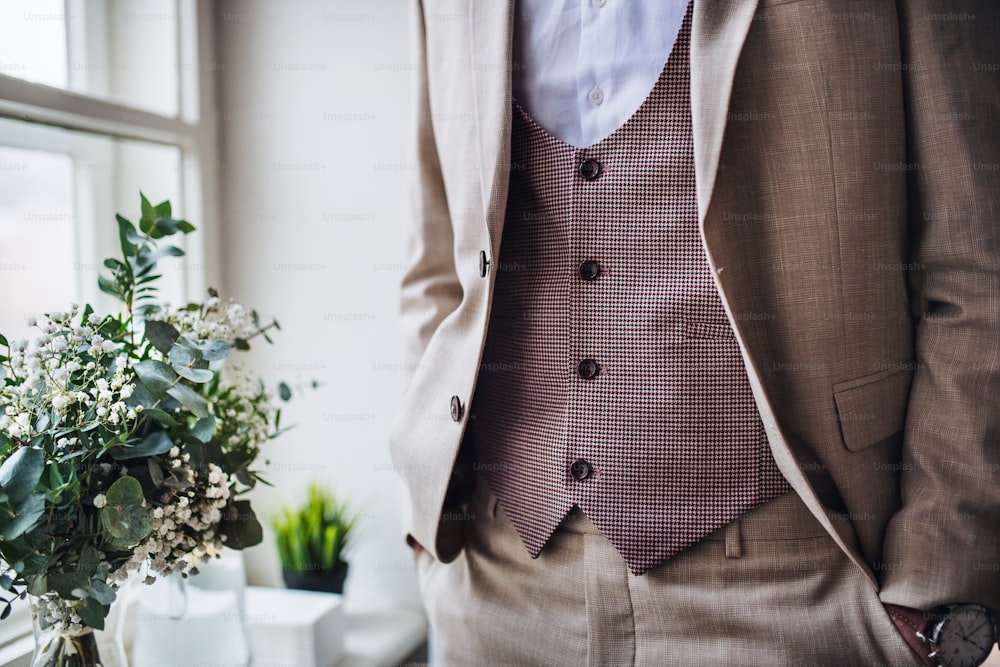 A midsection of man with formal suit standing on an indoor party, hands in pockets.