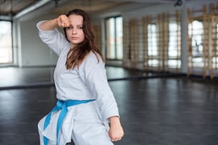 An attractive young woman practising karate indoors in gym.