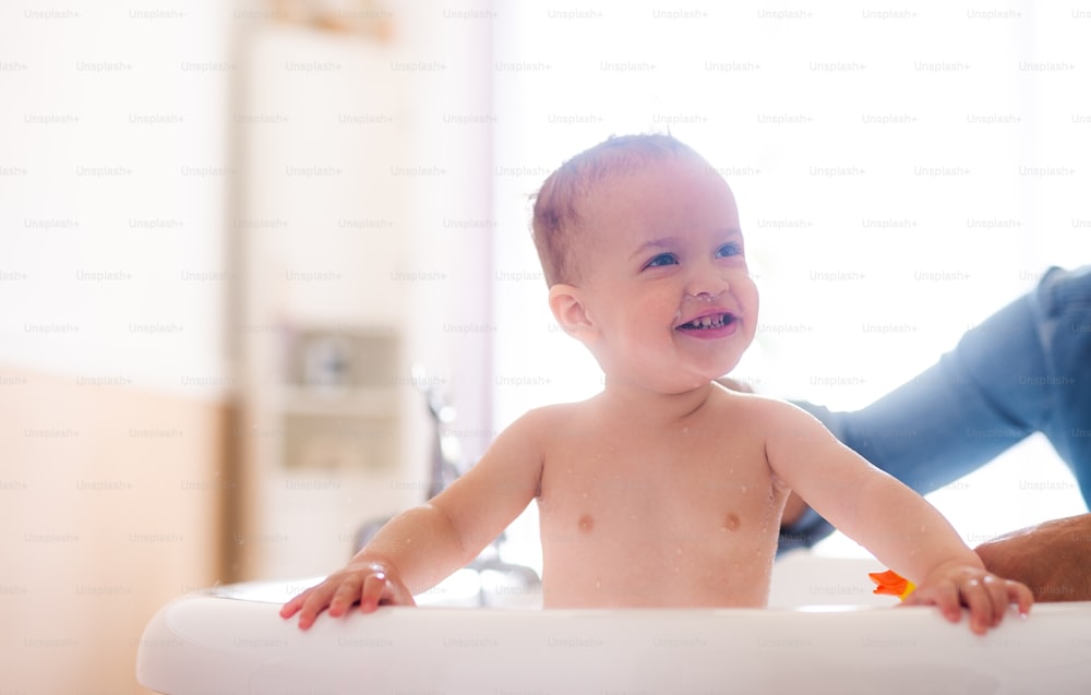 Padre irreconocible lavando a su hijo pequeño feliz en un baño en el interior de su casa.