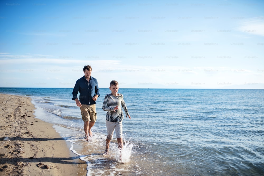 Padre con figlio piccolo durante una passeggiata all'aperto sulla spiaggia, correndo a piedi nudi nell'acqua.