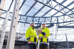 Front view of men engineers standing outdoors on construction site, using tablet.