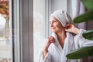 Front view portrait of woman with bathrobe and towel on head standing indoors at home.