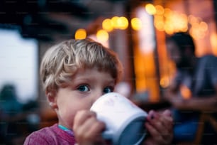 A close-up of toddler boy standing outdoors, drinking from cup.