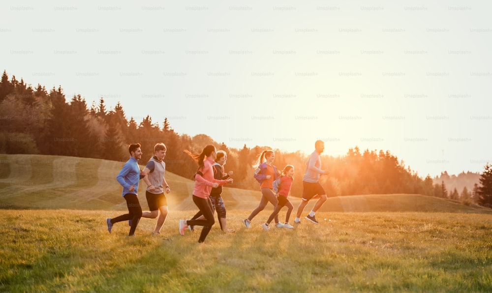 Um grande grupo de pessoas atravessa o país correndo na natureza ao pôr do sol.