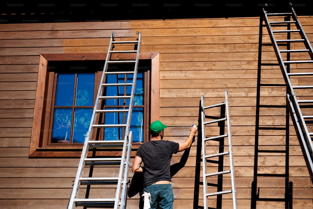 A mature man outdoors in summer, painting wooden house. Copy space.