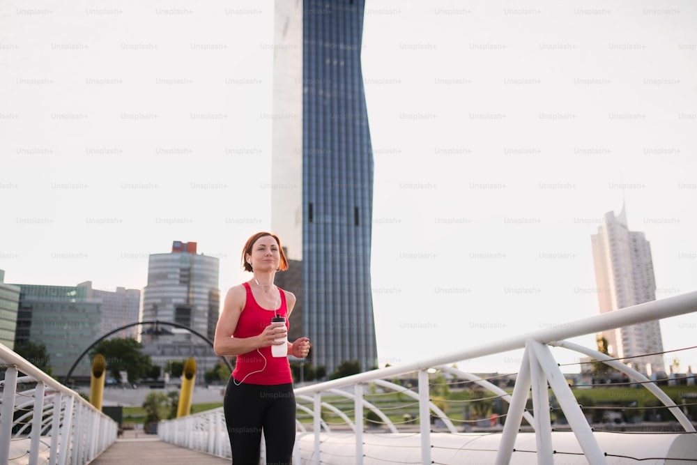 Front view of young woman runner with earphones jogging outdoors in city.