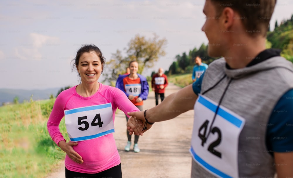 A man helping a pregnant woman in running competition in nature, giving her a hand.