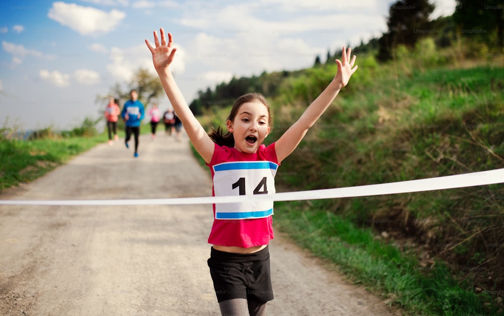 A small girl runner crossing finish line in a race competition in nature.