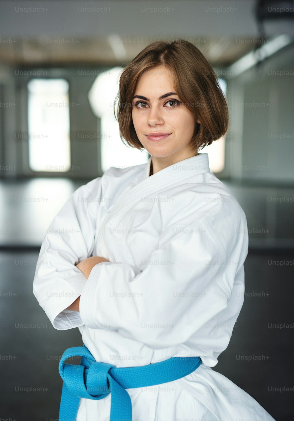 Eine junge Karate-Frau, die drinnen im Fitnessstudio steht und in die Kamera schaut.
