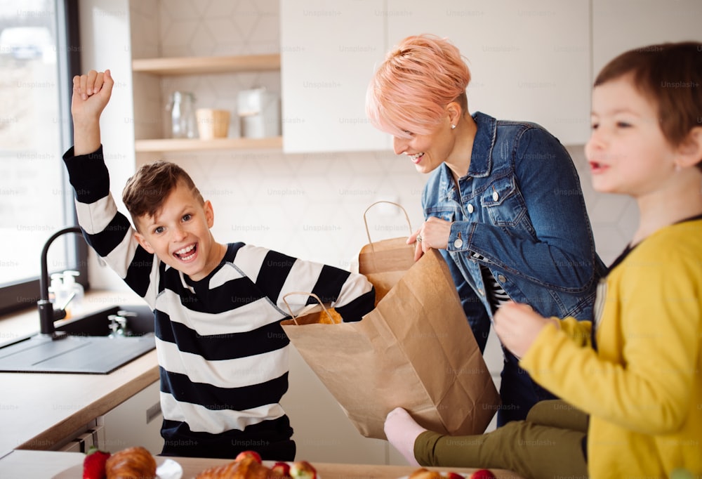 A happy young woman with two children unpacking shopping in a kitchen.
