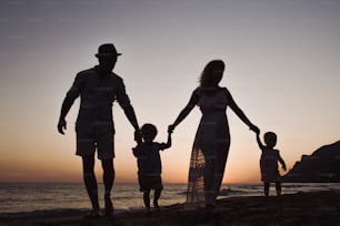 A family with two toddler children walking on beach on summer holiday at dusk, silhouettes holding hands.