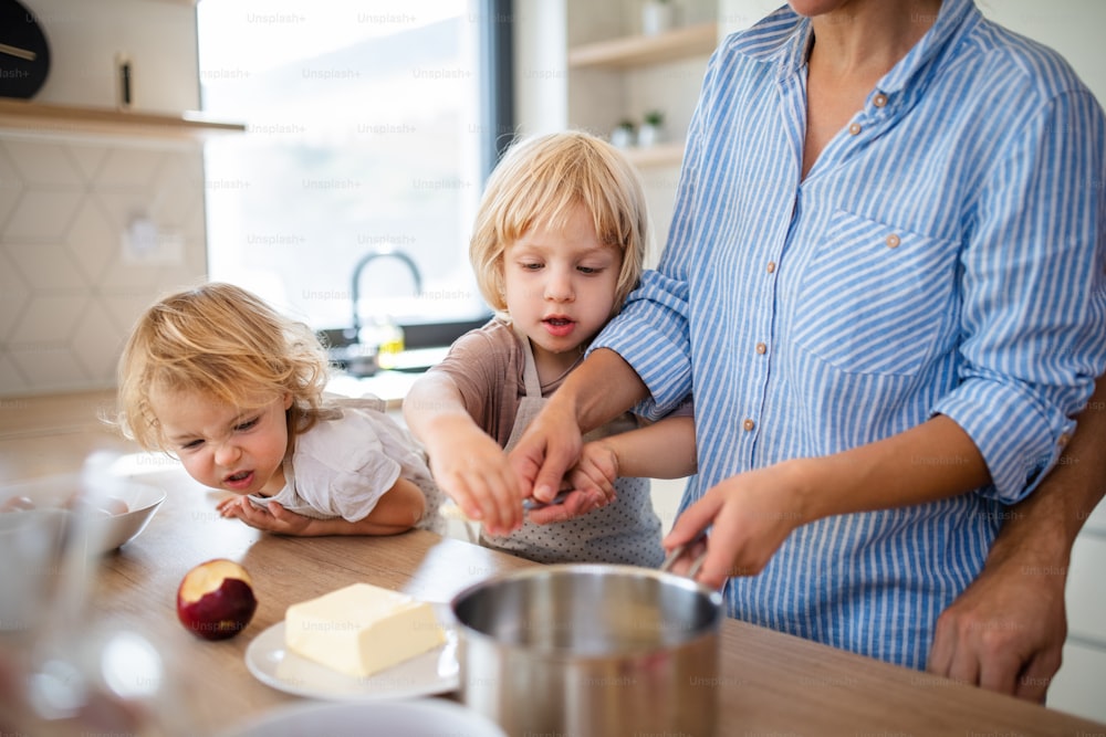 Uma jovem família com duas crianças pequenas dentro de casa na cozinha, preparando comida.