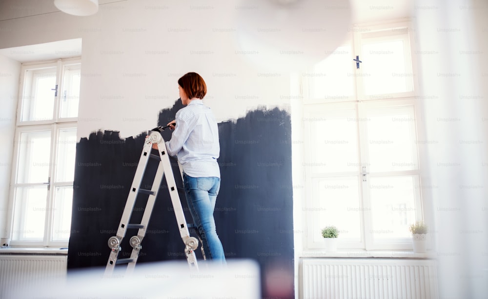 Una joven mujer creativa pintando la pared de negro. Una startup de pequeña empresa.