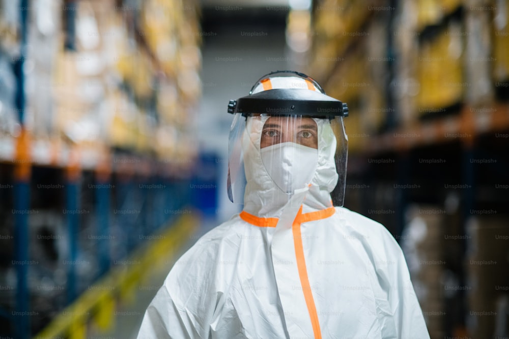 Front view of worker with protective mask and suit in industrial factory, looking at camera.