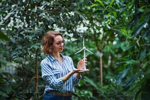 Mujer joven de pie en el jardín botánico, sosteniendo el modelo del molino de viento. Espacio de copia.