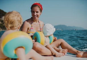 Una madre y dos niños pequeños con brazaletes sentados en la playa durante las vacaciones de verano.